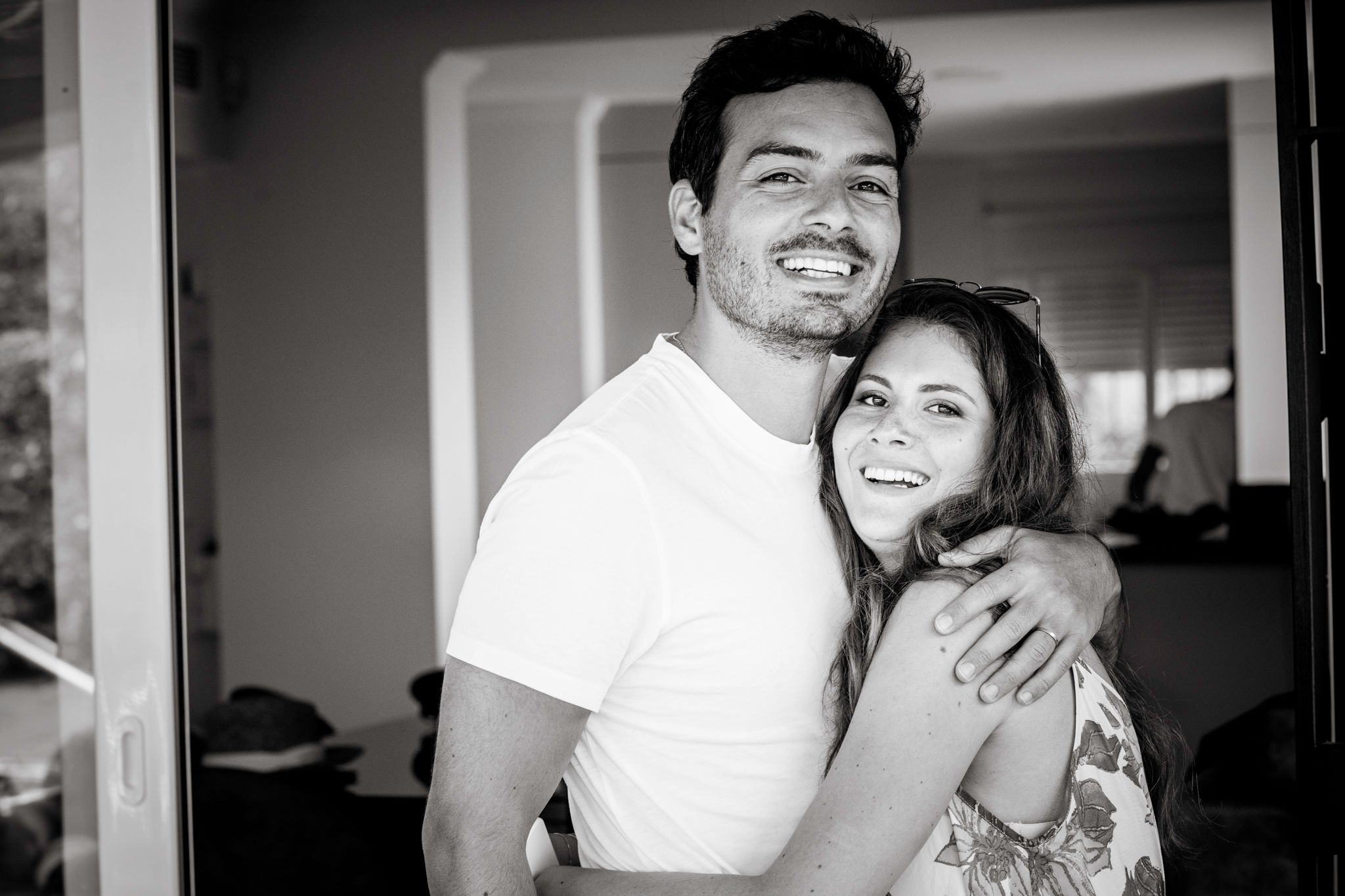 A black-and-white photo of a couple hugging and looking to the camera.
