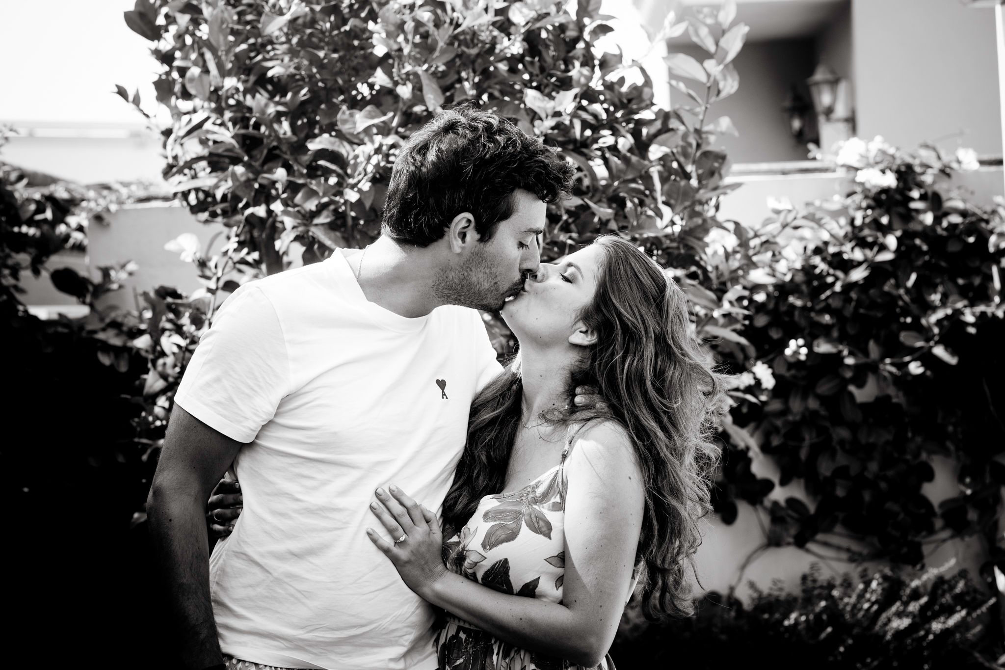 A black-and-white photo of a couple kissing and the woman put her left hand on the tummy of her husband.