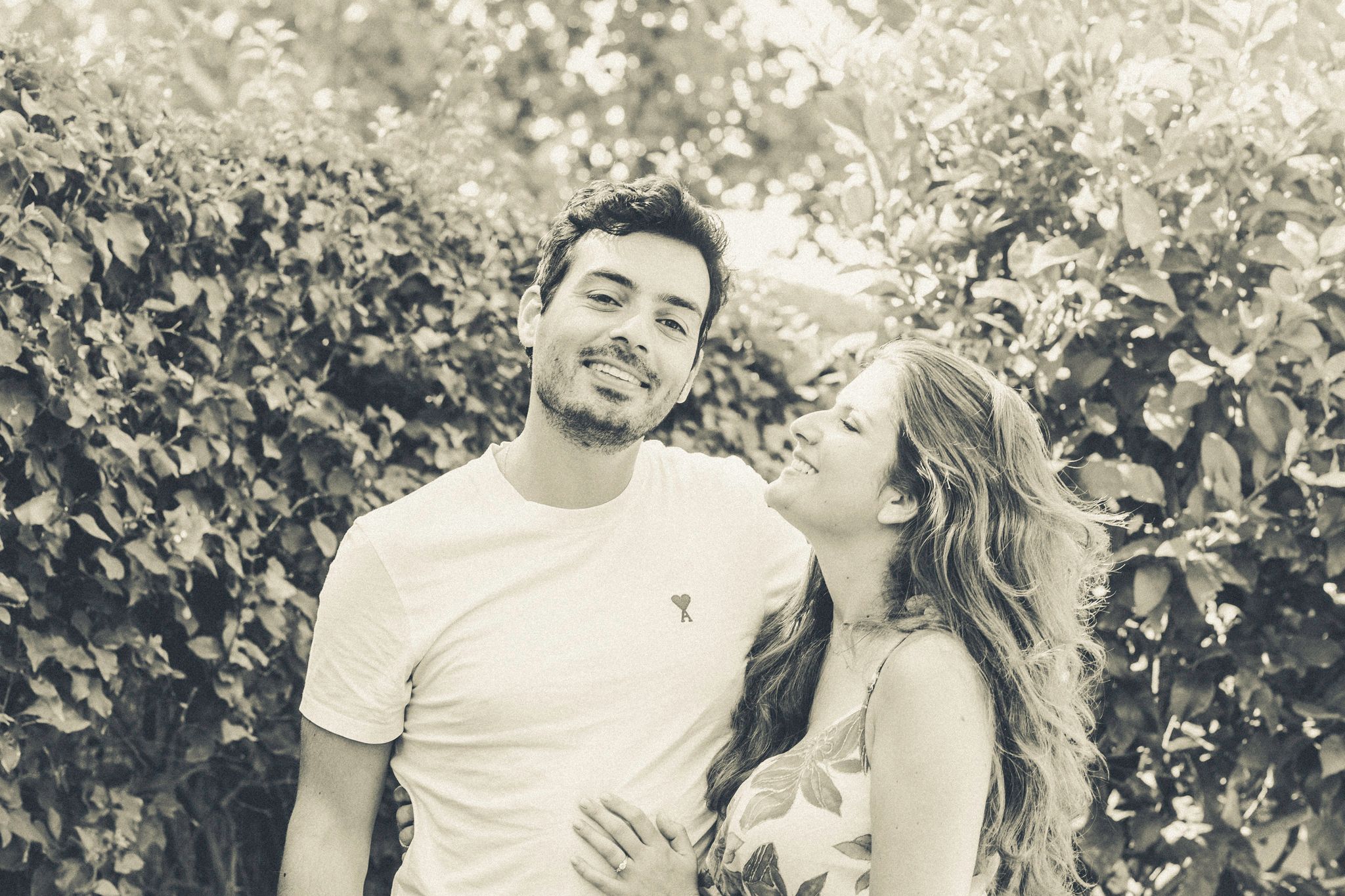 A black-and-white vintage old style photo of a couple, she is looking at him, he is looking to the camera.