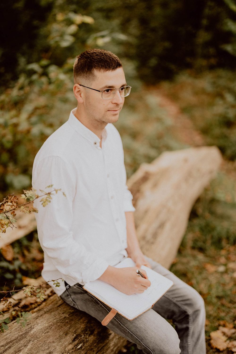 Person in white shirt and glasses sitting outdoors during an autumn photo session.