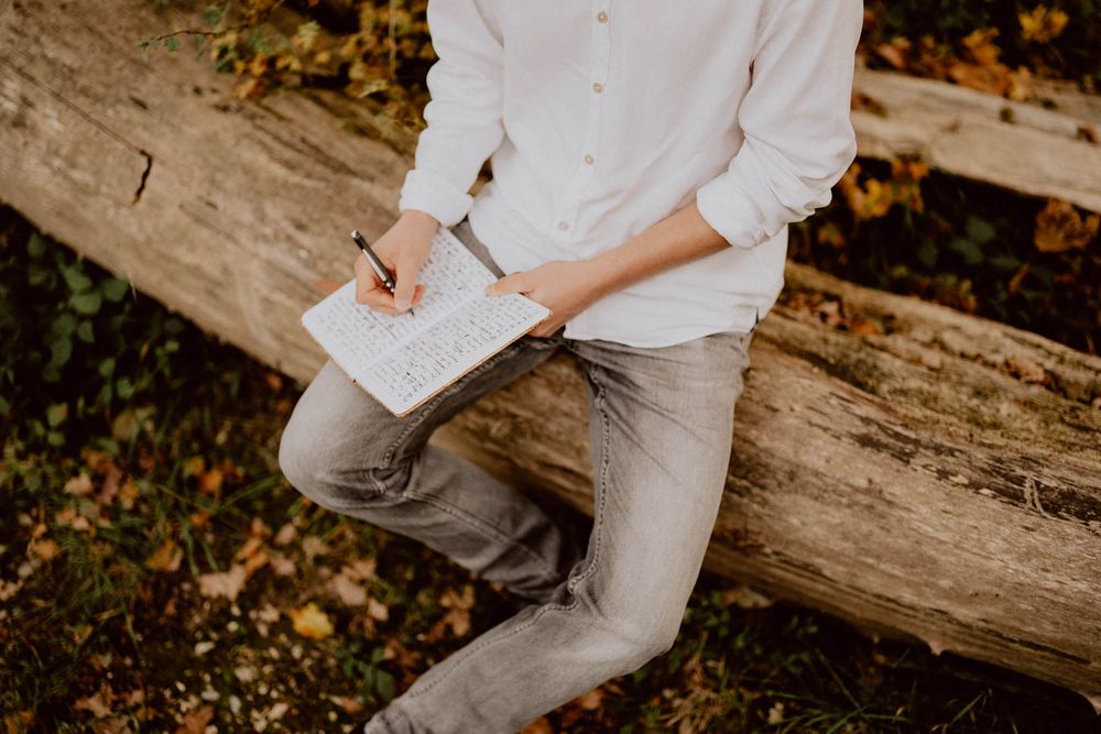 Person in white shirt sitting on rustic wooden log during autumn photoshoot.