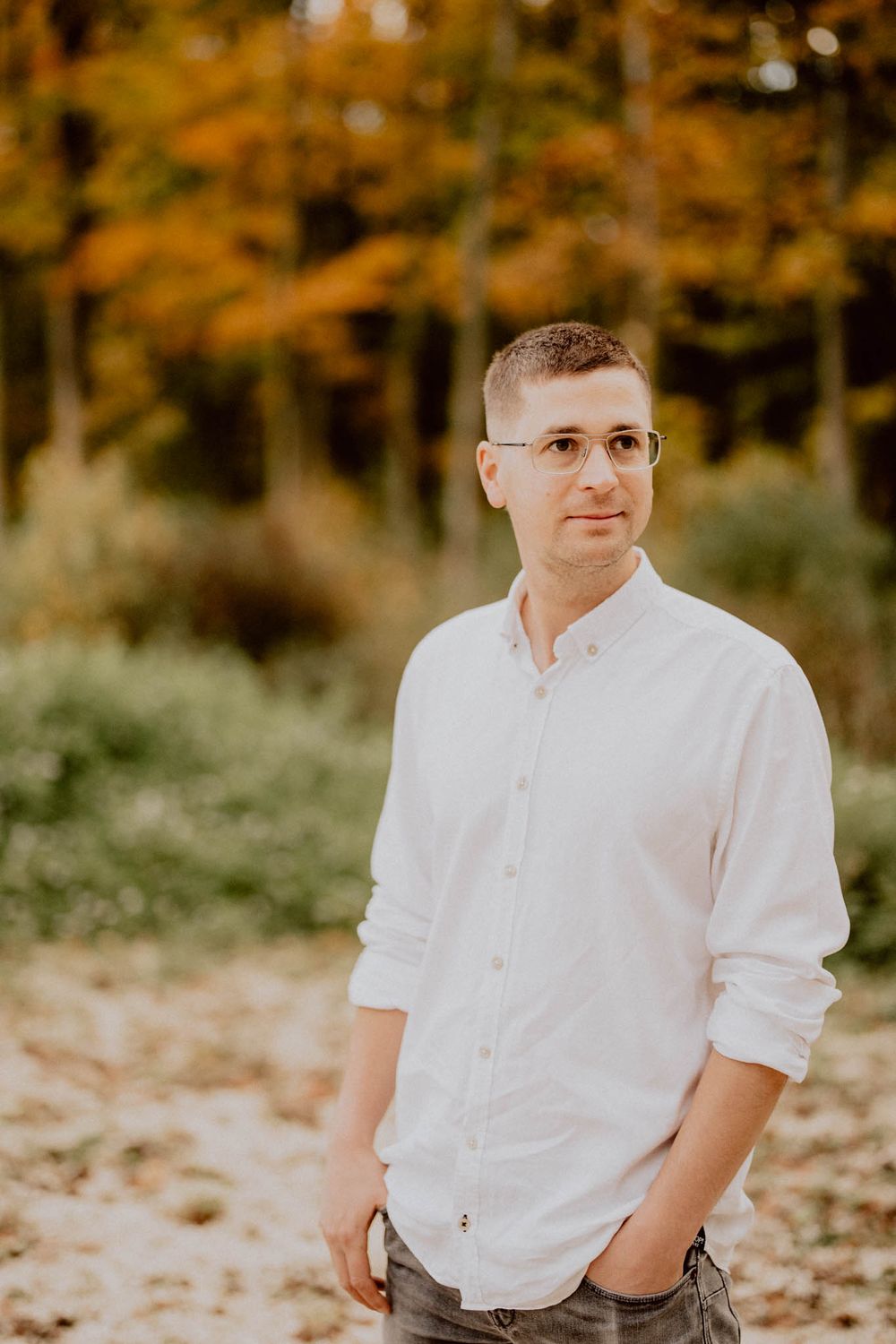Portrait in autumn setting wearing a white button-down shirt and glasses.