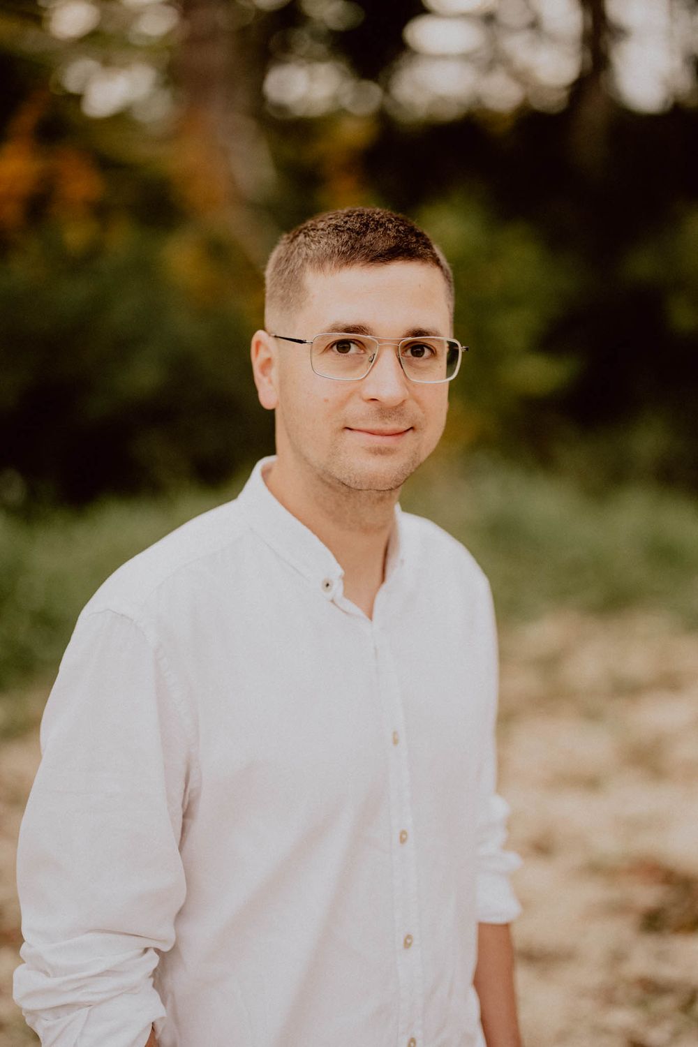 Portrait series showing a person in a white button-up shirt against a soft focused natural background.