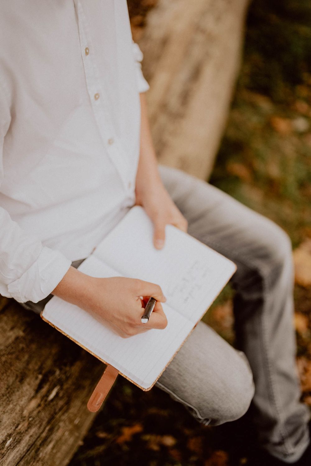 Close-up shot of hands writing in a white notebook while sitting on a wooden surface.