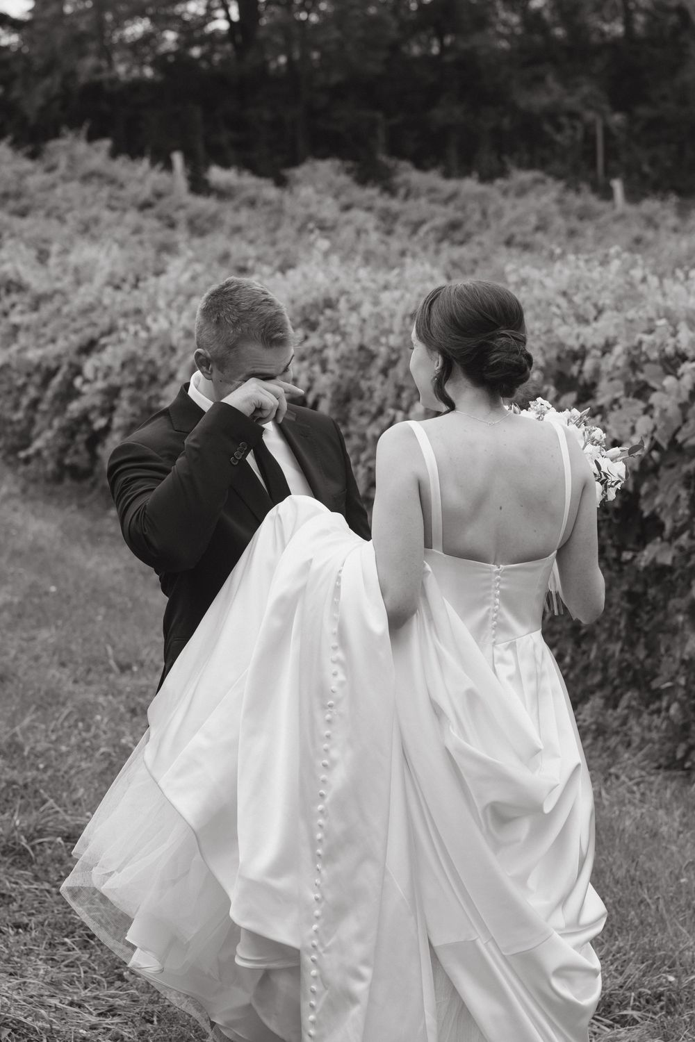 Row of bridesmaids in white dresses walking together showing the back details of their gowns.