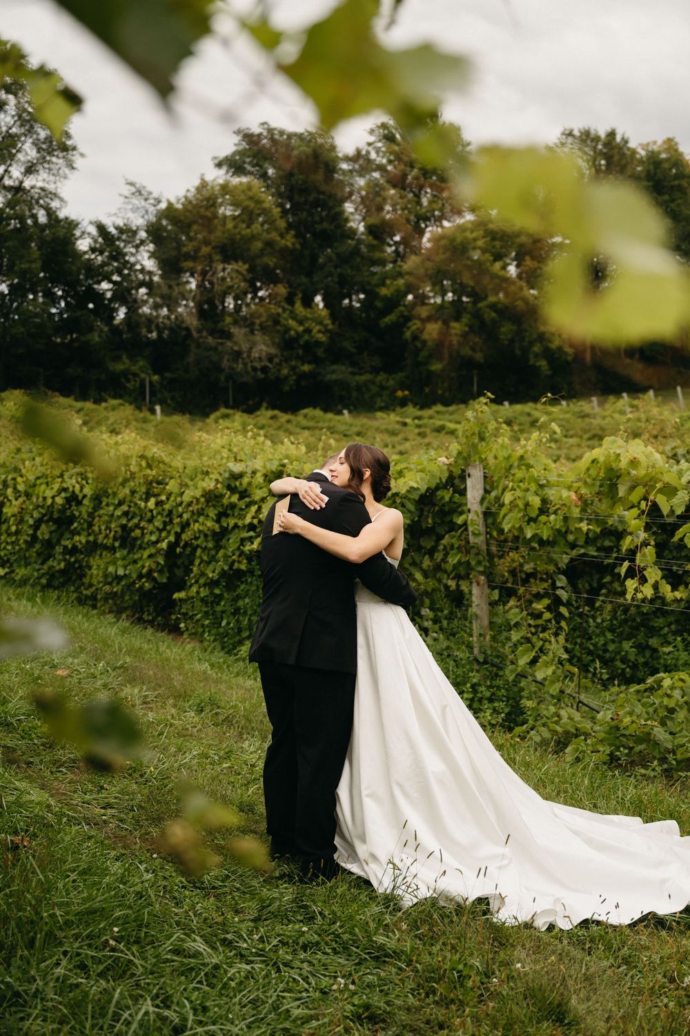 Wedding couple embraces in a romantic pose among lush green vineyard rows.
