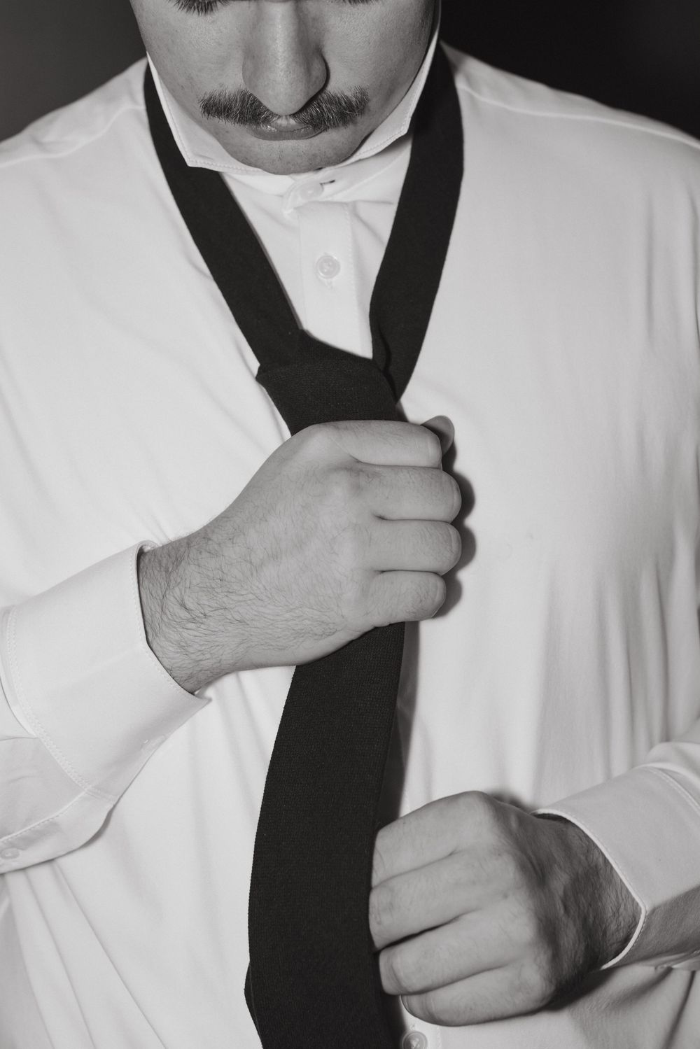 Close-up sequence showing hands tying a black necktie against a white dress shirt.