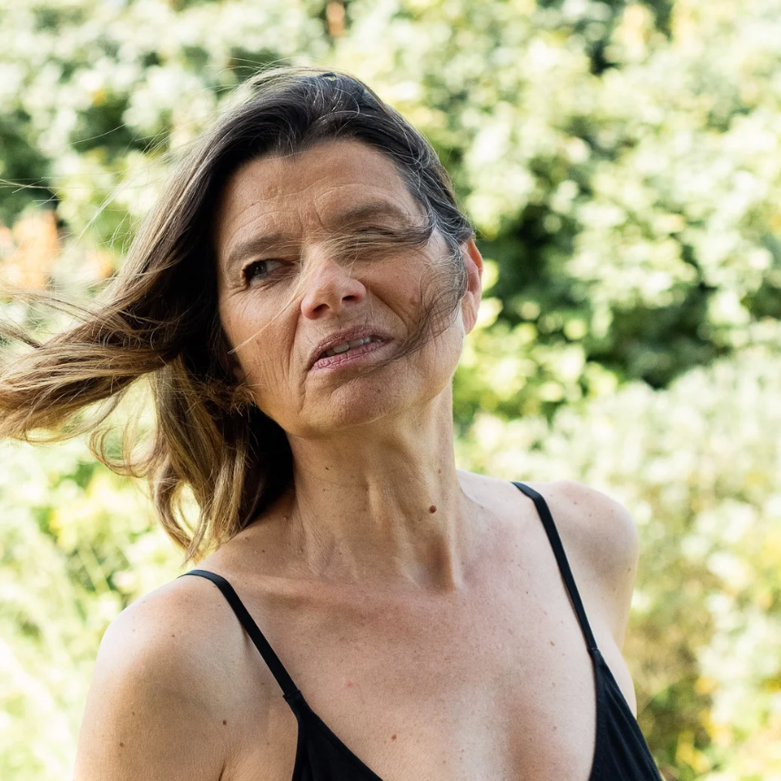A candid summer portrait with wind-blown hair against lush greenery.
