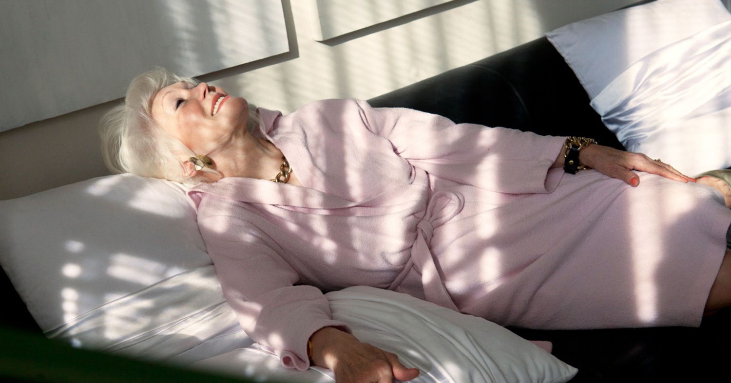 Person in pink clothing lying down in dramatic sunlight and shadow.