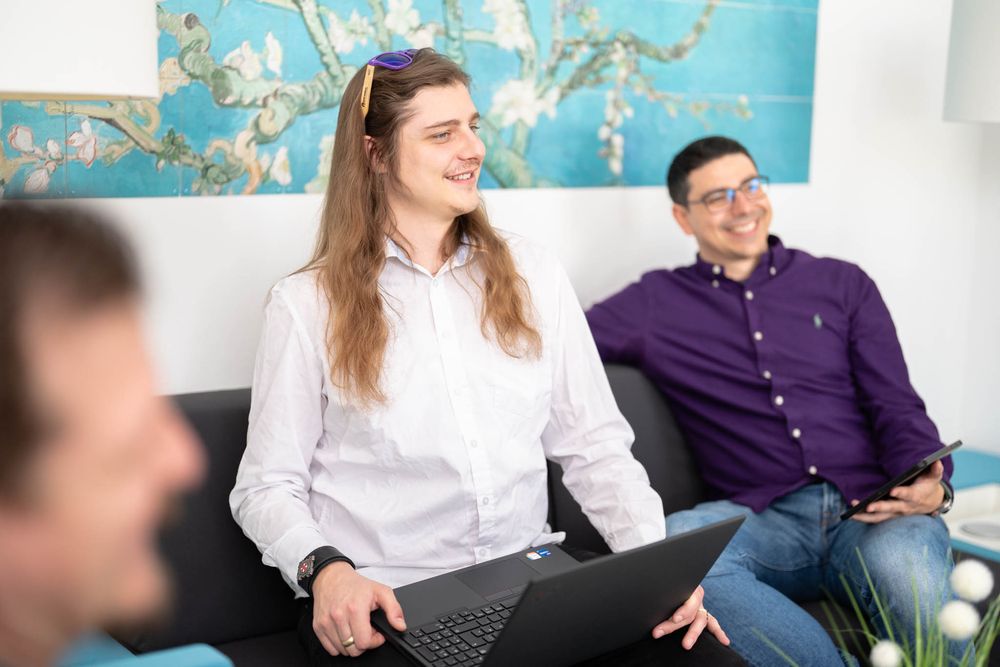 People sitting on a couch during a casual meeting with a laptop and decorative artwork on the wall behind them.