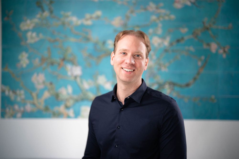 Professional headshot portrait against a turquoise and gray textured wall background.