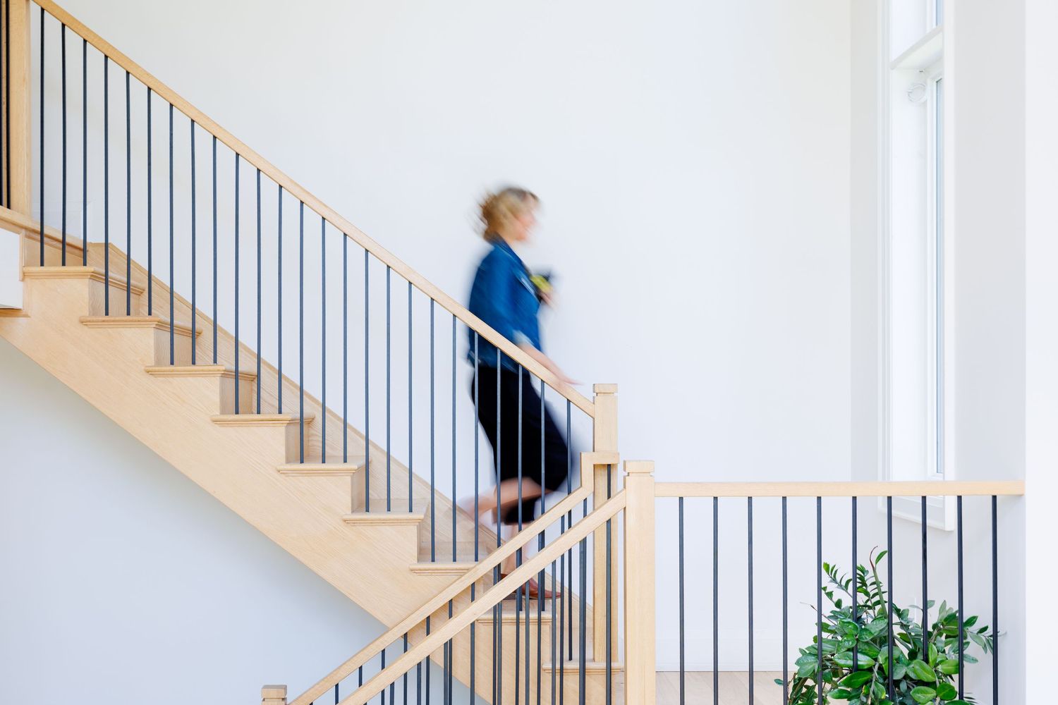 Person walking up light wooden staircase with metal railing and white walls in modern minimalist interior design.