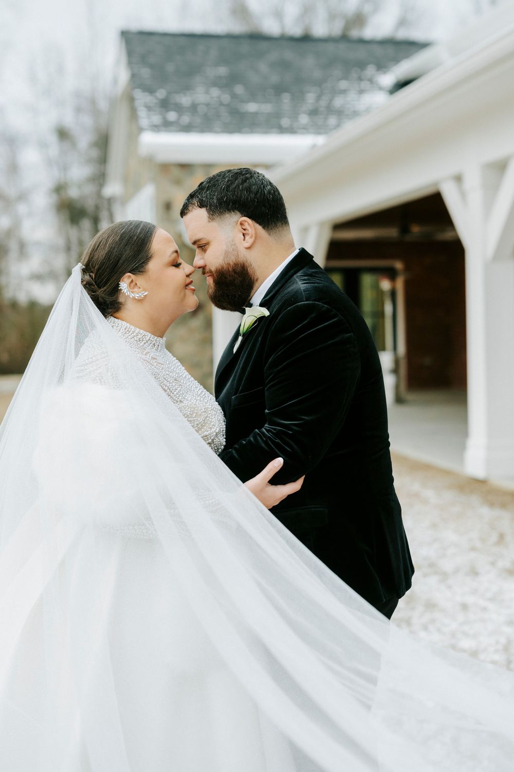 Romantic wedding couple embracing under a flowing white veil in a winter setting.