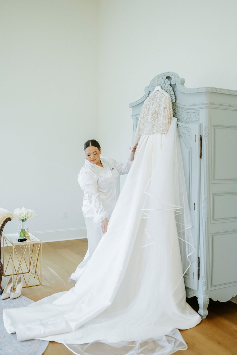 Wedding dress with long train displayed in an elegant white room with hardwood floors.