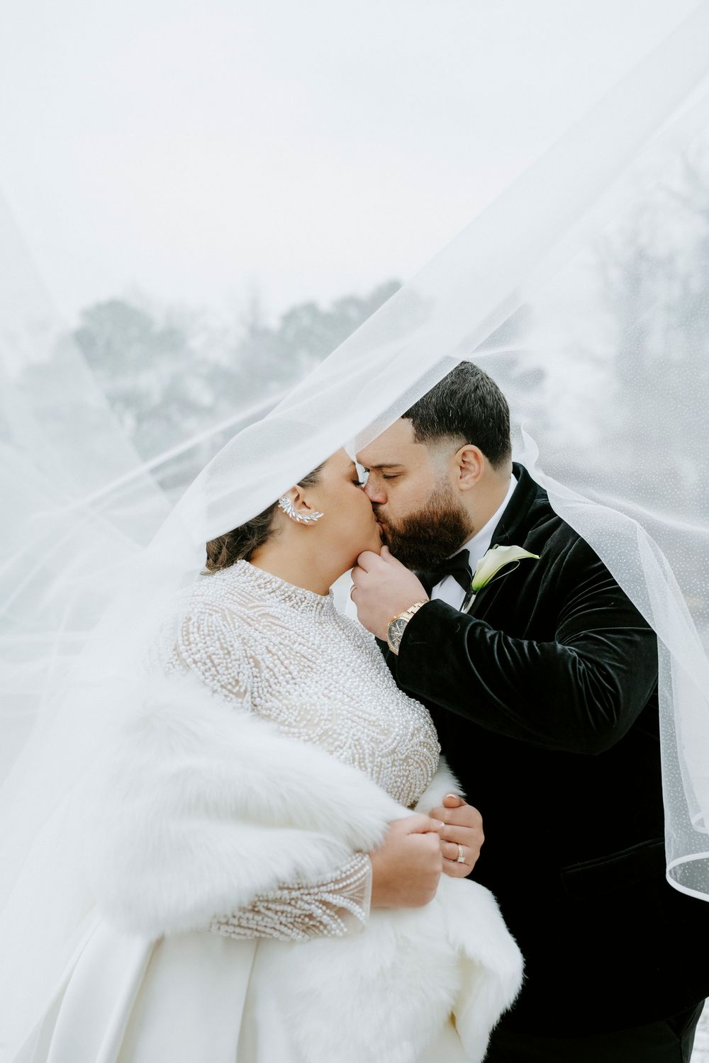 Intimate winter wedding moment captured with flowing veil and formal attire in snowy setting.