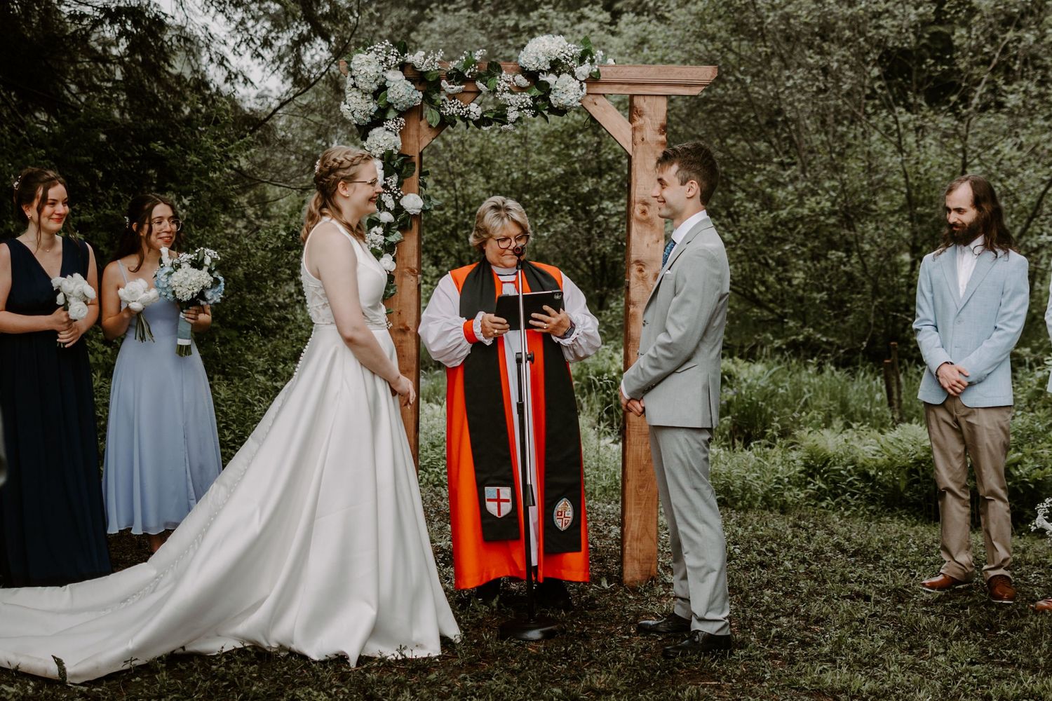 Bride and groom laughing with officiant at outdoor woodland wedding ceremony altar.
