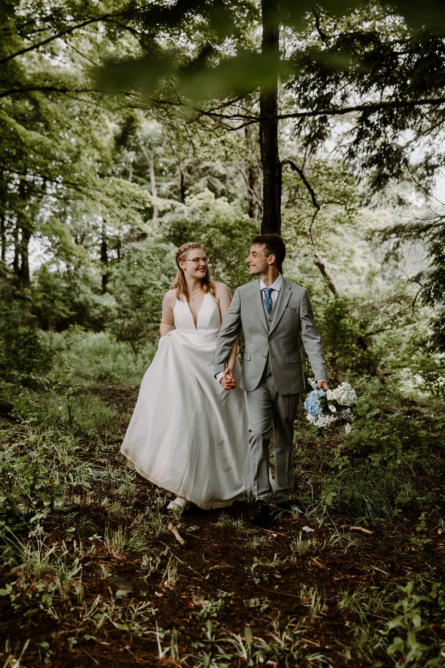 Bride and groom walking hand in hand through lush forest on wedding day.