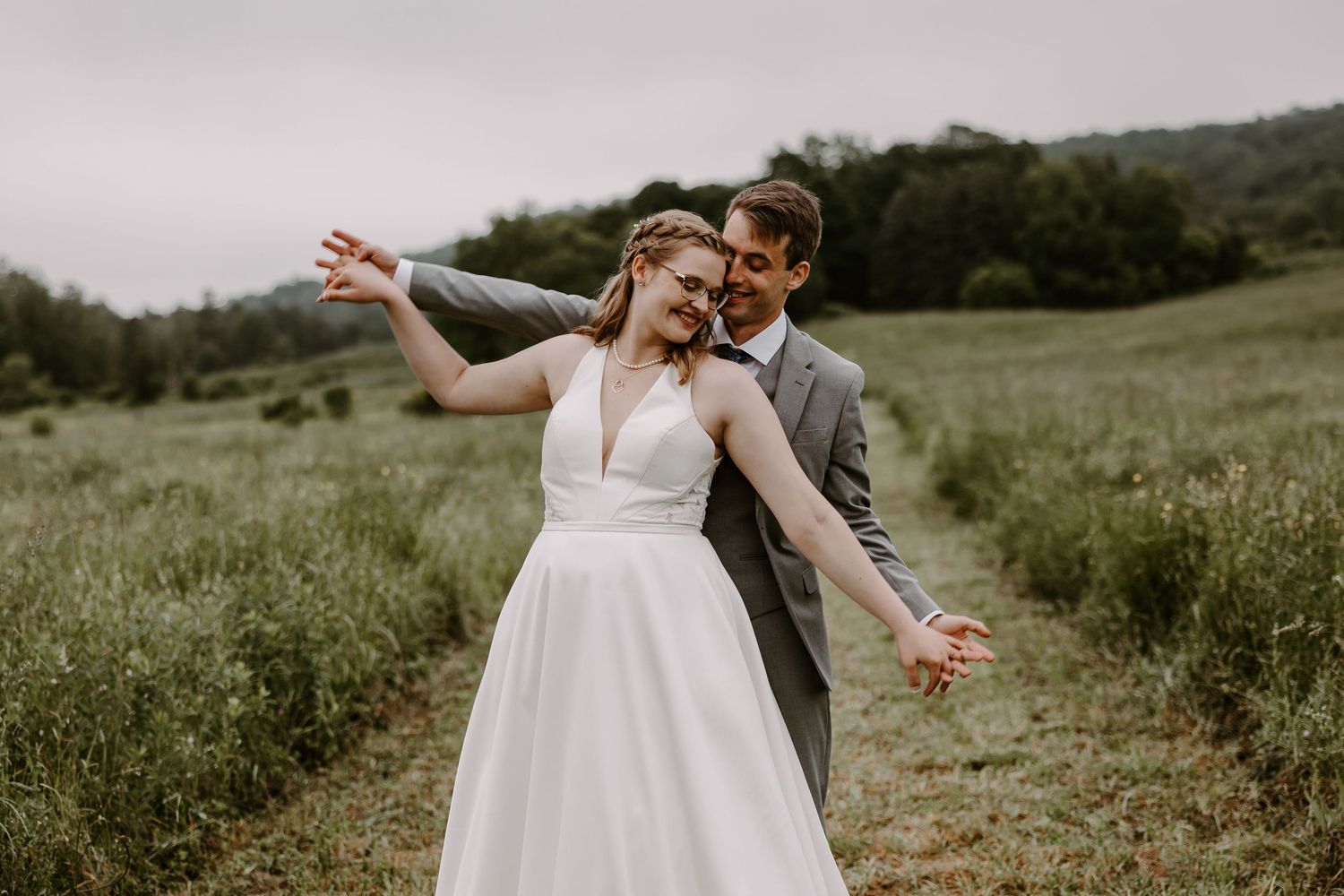 Bride and groom dancing joyfully in green meadow on their wedding day.