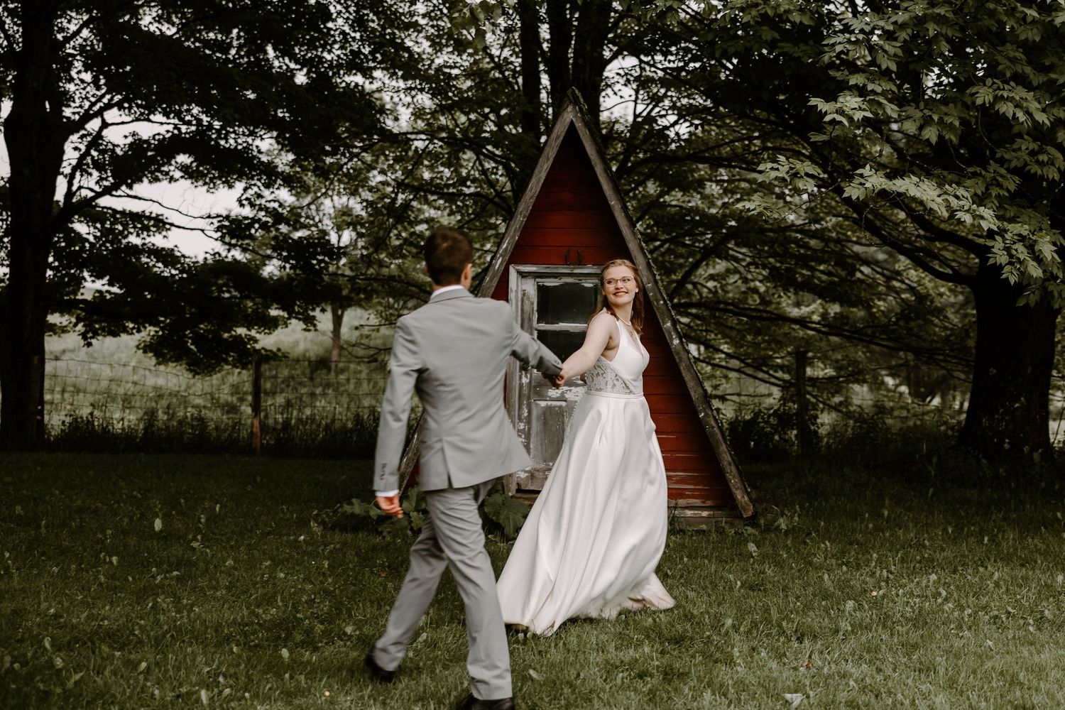 Bride and groom dancing near rustic A-frame cabin surrounded by trees.