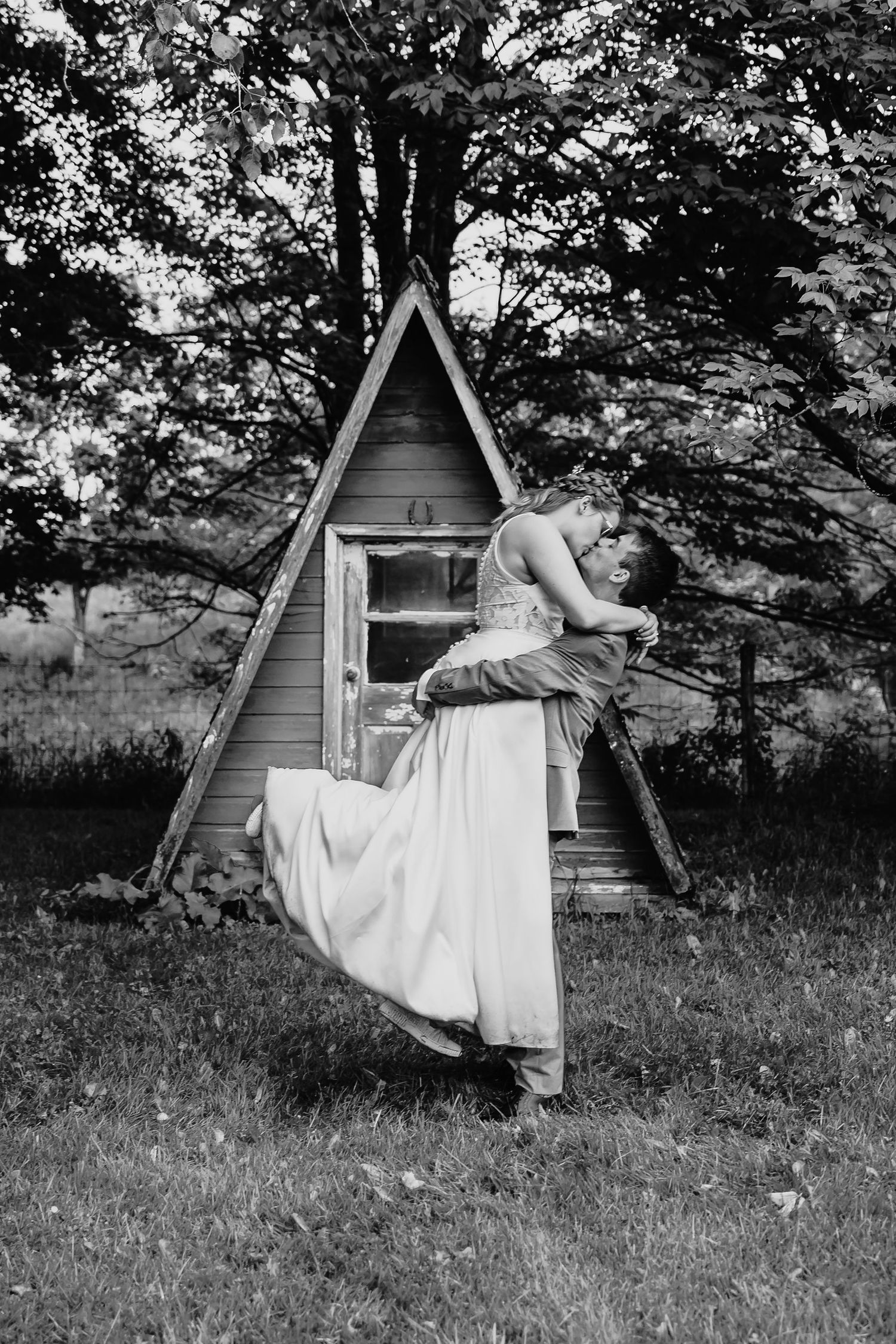 Groom lifting bride in romantic black and white photo near A-frame cabin.