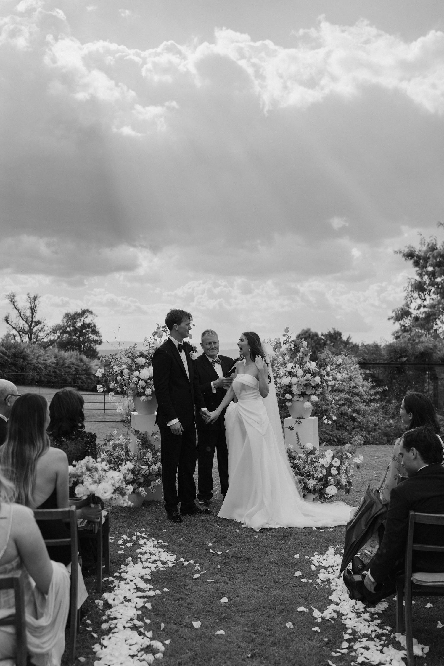 sun rays streaming through the clouds as bride and groom laugh with each other during wedding ceremony at dewsall court in herefordshire