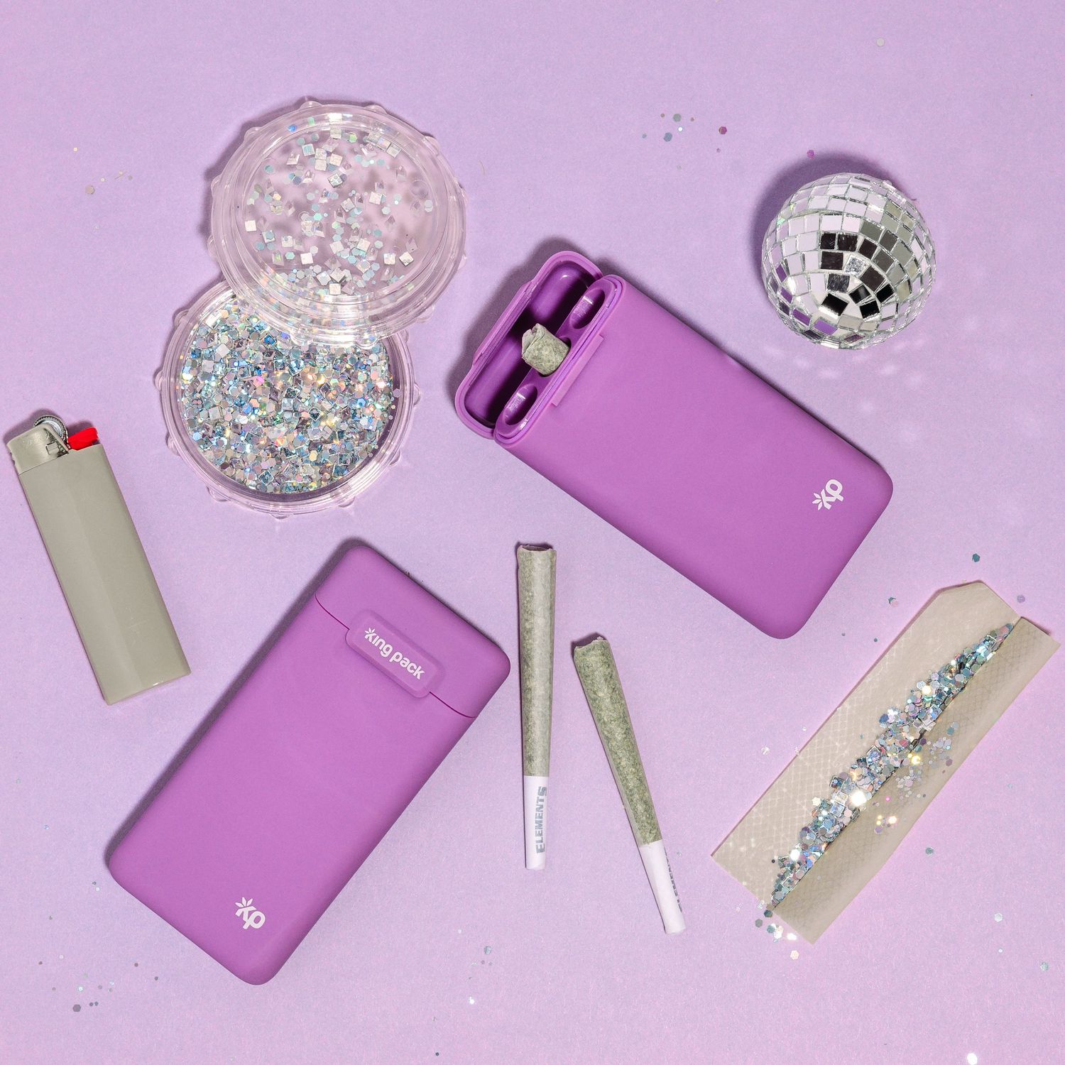 Flatlay of pink vaping devices and accessories with glittery decorative elements on a purple background.