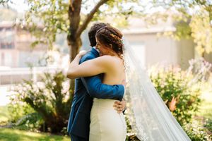 A couple embraces in a sunlit garden setting during their wedding celebration.