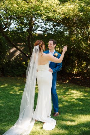 A couple shares their first dance outdoors on a sunny day, with the bride wearing a flowing white gown and long veil.