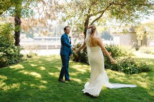 A couple in wedding attire walks through a sunlit garden setting during an outdoor photo session.