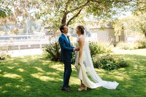 A couple shares a romantic moment on their wedding day in a lush green outdoor setting.
