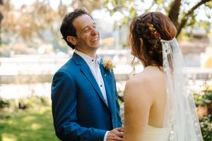 A joyful moment between a couple on their wedding day, with the groom in a blue suit and bride in white outdoors.