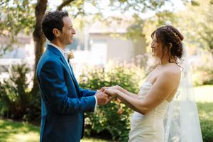 A couple in wedding attire shares a playful moment while dancing together in a sunlit outdoor garden setting.