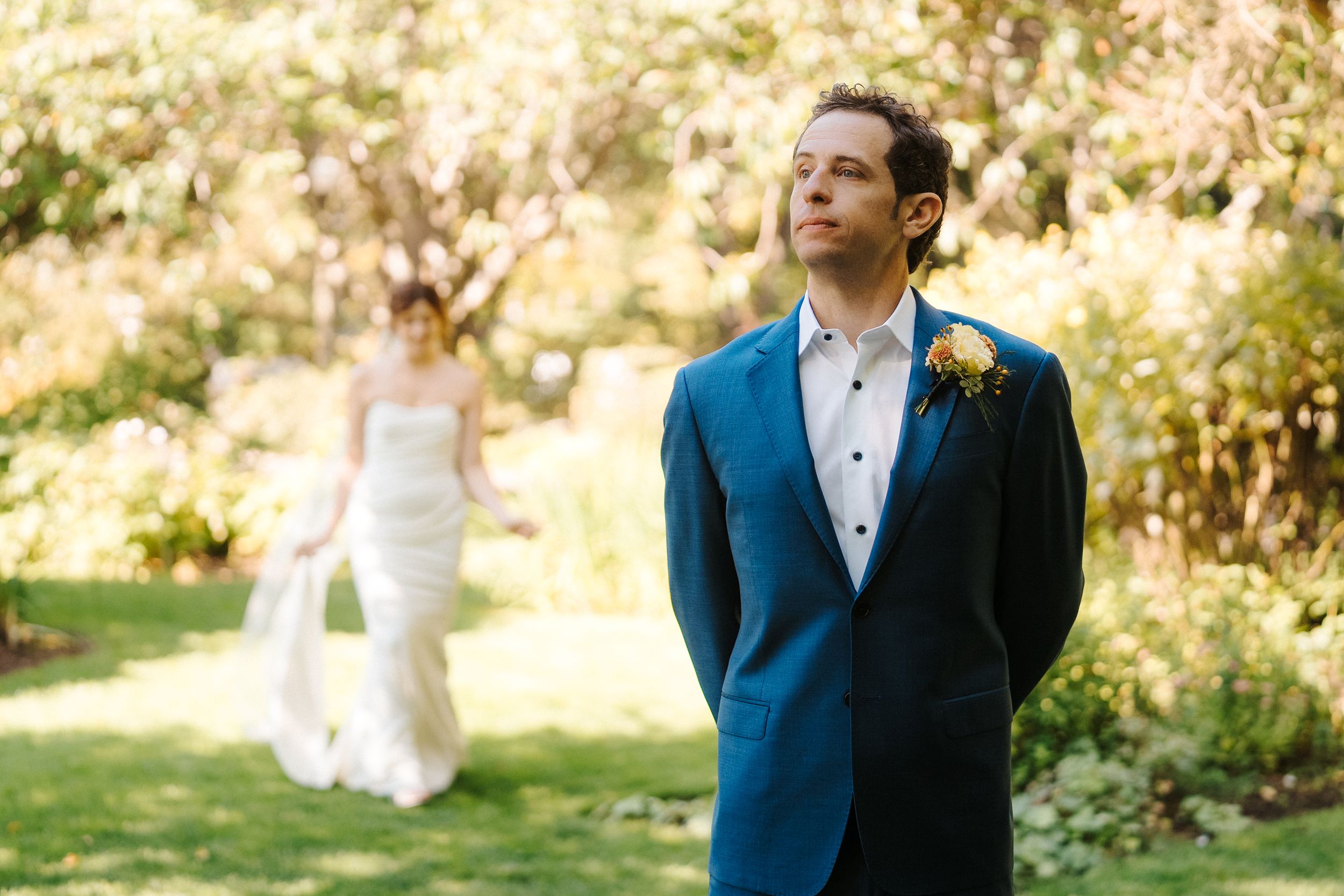 A wedding couple walks through a sunlit garden path while sharing romantic moments in elegant attire.
