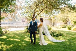 A couple strolls through a lush garden setting with golden sunlight filtering through the trees.