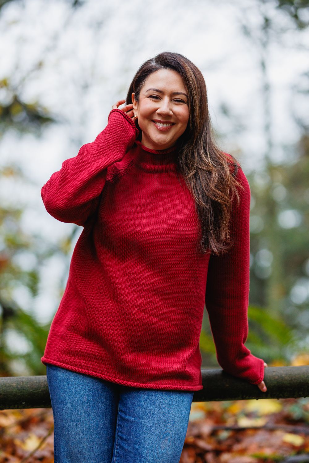 Cheerful woman in red turtleneck sweater leaning on a fence rail in an autumn park.