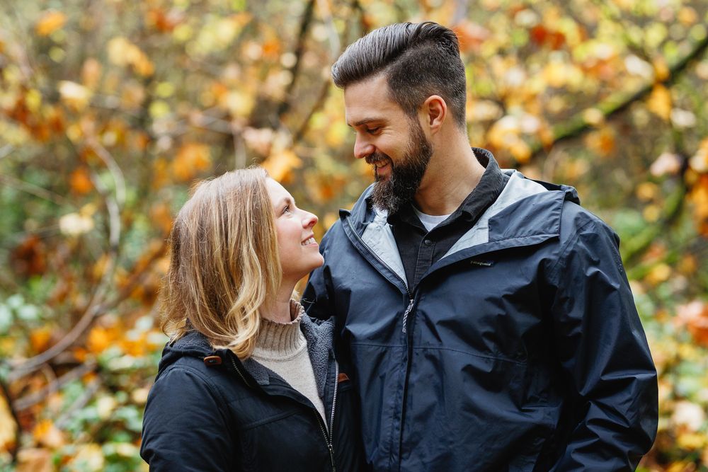 Smiling couple gazing at each other with colorful fall foliage behind.