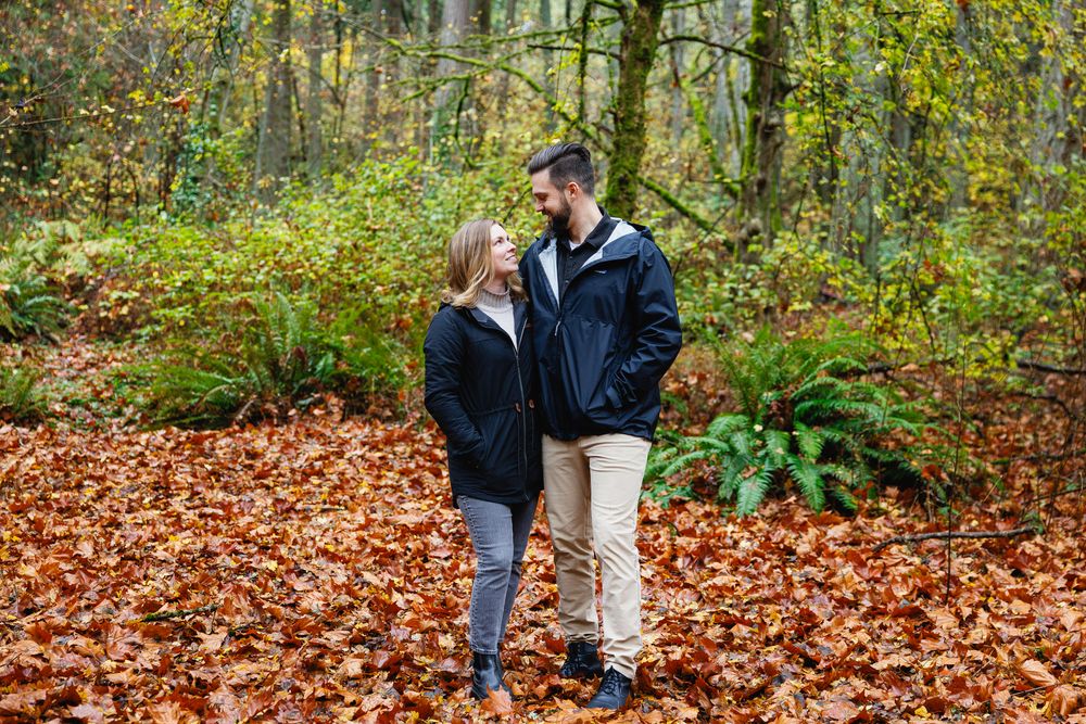 Couple standing face to face on a carpet of orange autumn leaves in a woodland.