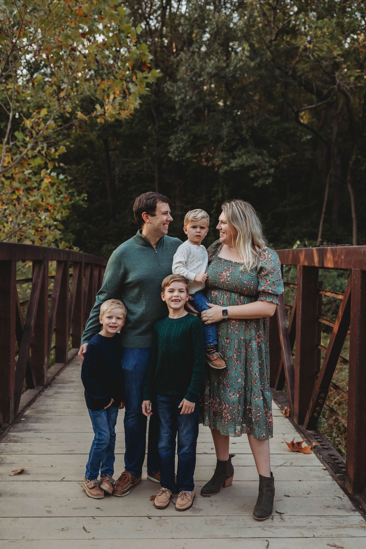 A happy family of five poses together on a wooden bridge surrounded by autumn foliage.