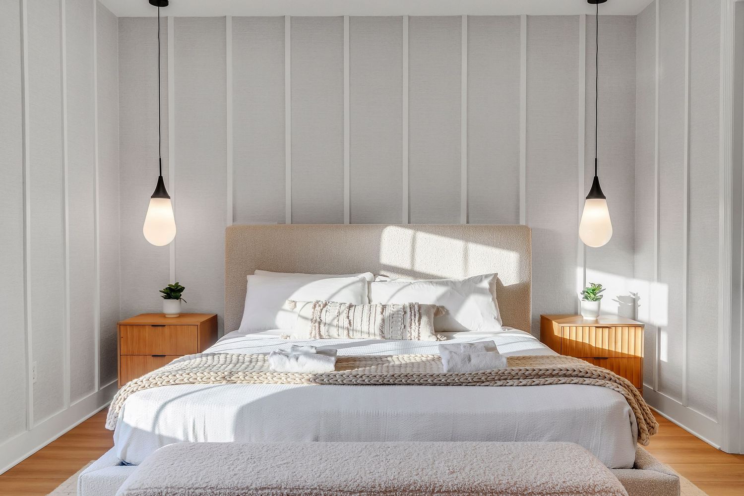Modern bedroom interior with white walls, pendant lights, and cozy bedding in neutral tones. real estate photograpphy