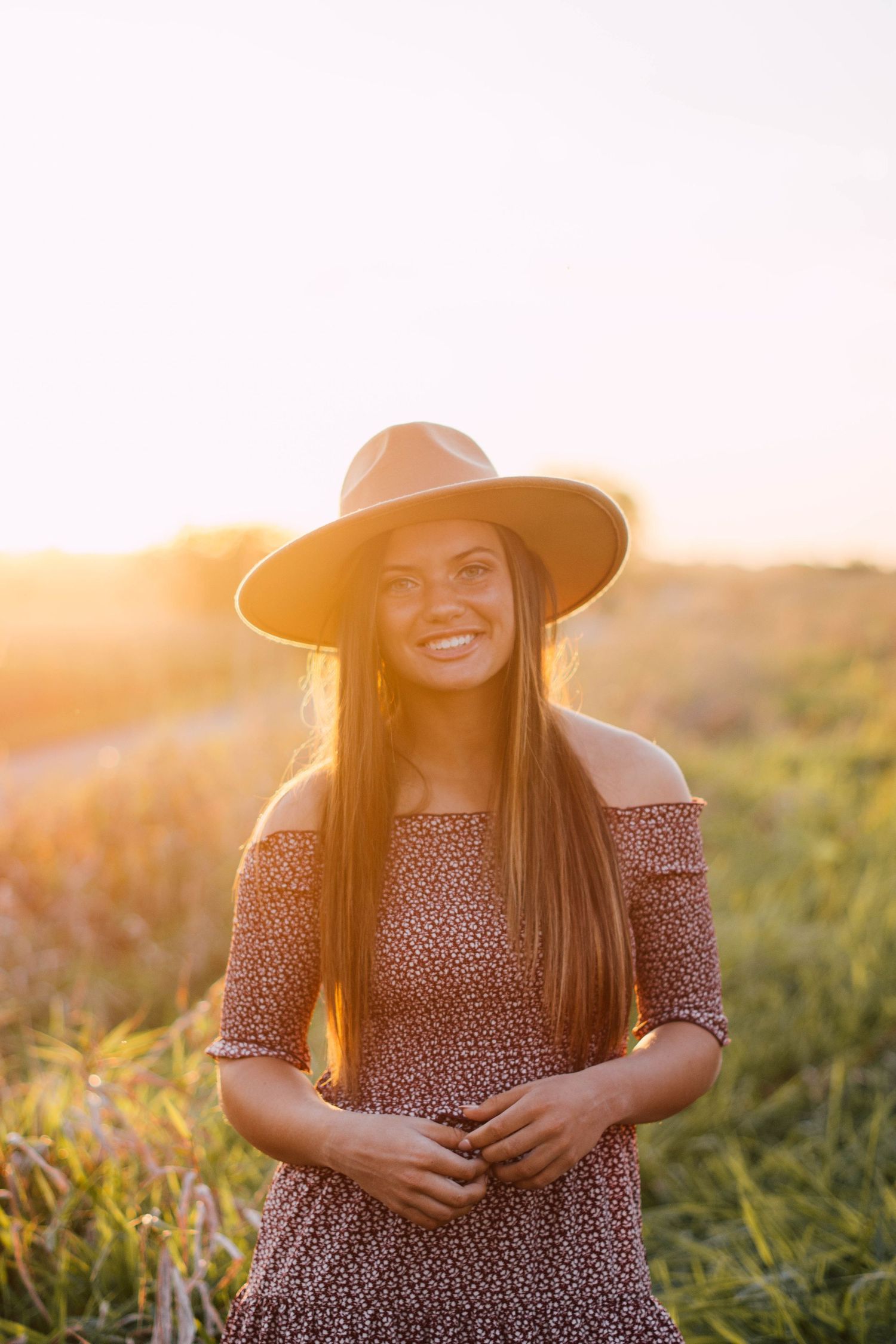 Portrait in brown hat and floral dress during golden hour in field.