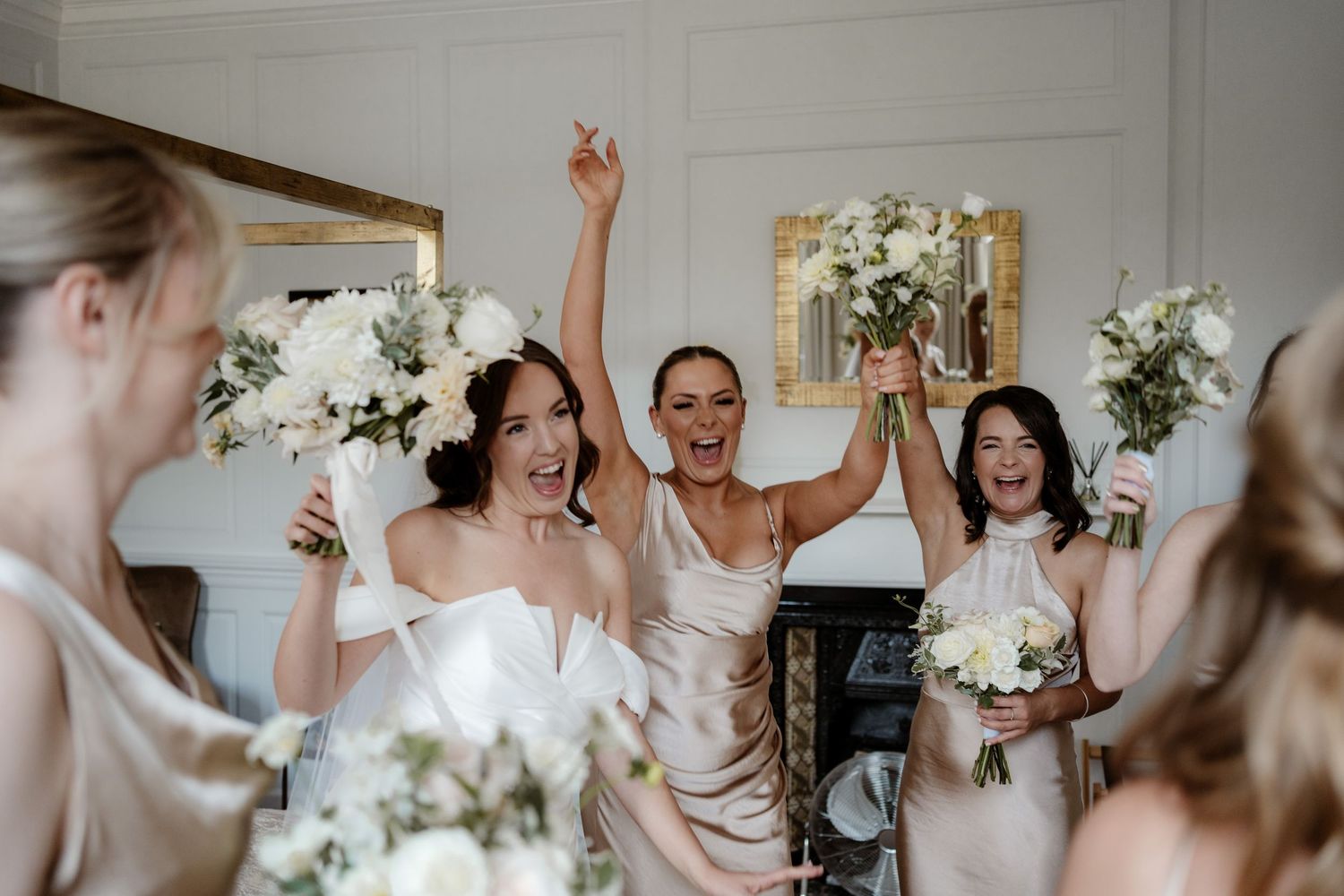 A series of candid moments captured in a bright white room with wooden floors and a chandelier during wedding preparations.