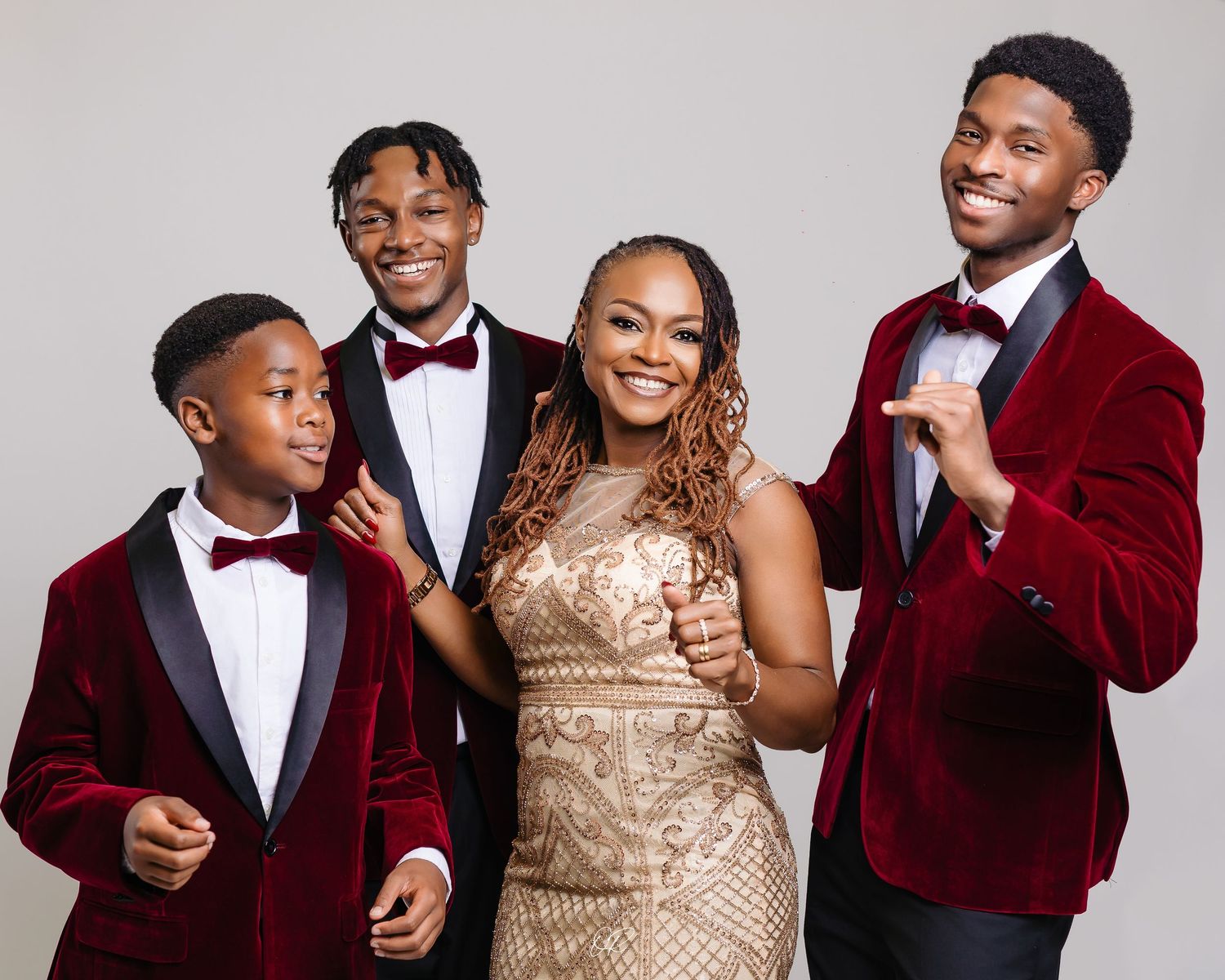 Family dressed in formal attire with red velvet blazers and gold sequin dress pose together for portrait.