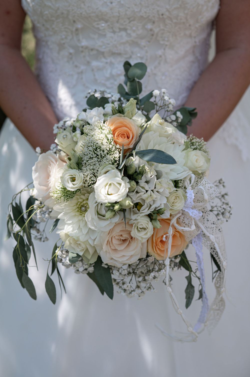 Ein zarter Brautstrauß aus weißen und pfirsichfarbenen Rosen mit Schleierkraut und Eukalyptusblättern.