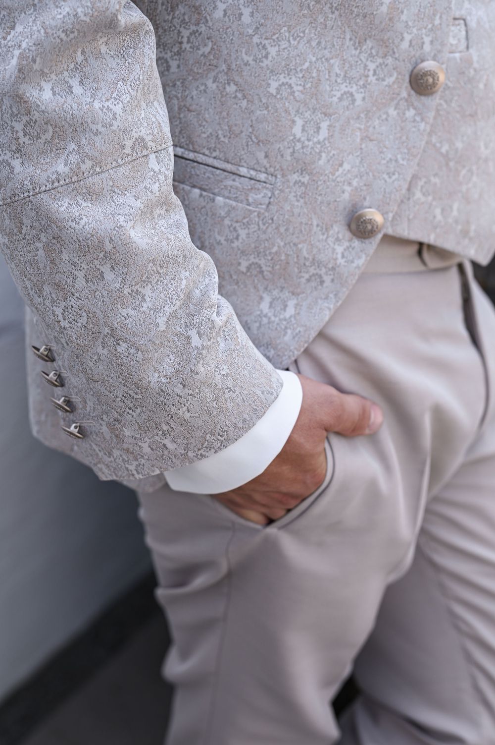 Nahaufnahme einer eleganten Hochzeitsanzugsjacke mit Zierknöpfen und passender heller Hose.