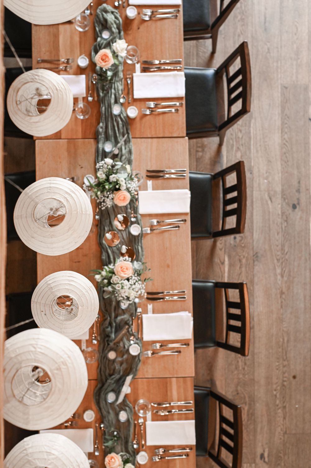 Elegant gedeckter Tisch mit weißen Gedecken, dunklen Holzstühlen und einem Eukalyptus-Blumenläufer in der Mitte.