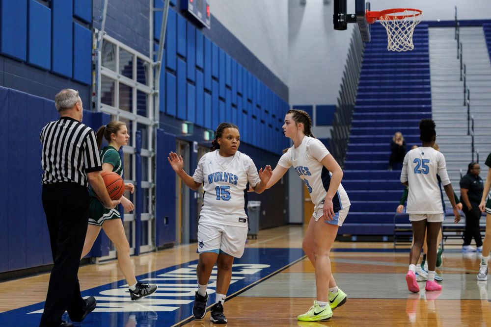 Basketball players await referee decision during game on blue court.
