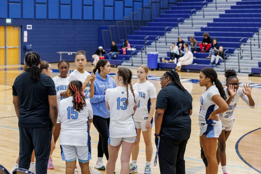 Basketball team gathers on court for strategic discussion during game break.