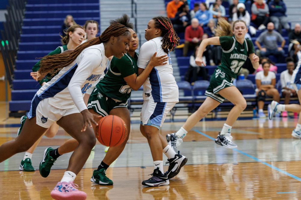 Basketball players compete for possession of the ball during an intense game on a blue court.