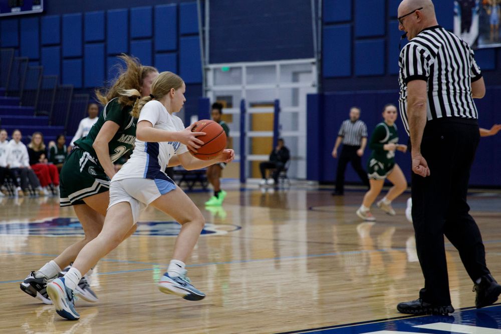 Basketball players battle for control of the ball while a referee observes the action.