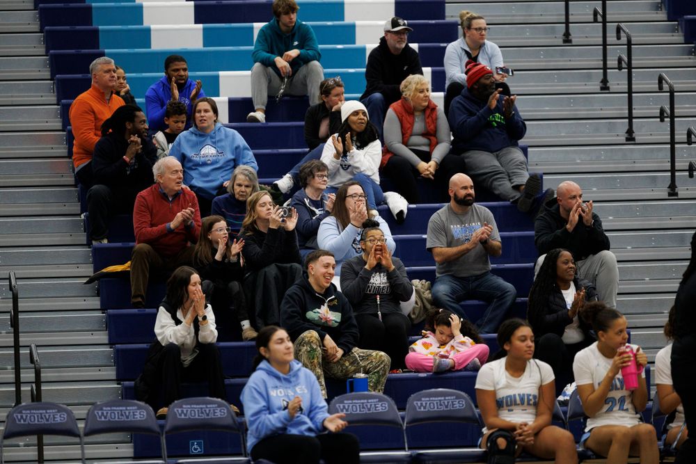 Spectators fill blue bleachers to watch a sporting event in an indoor gymnasium.
